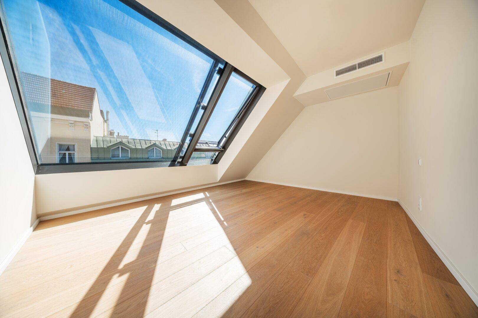 Heller Raum mit Holzboden und großem, schrägen Fenster, das viel Tageslicht spendet.