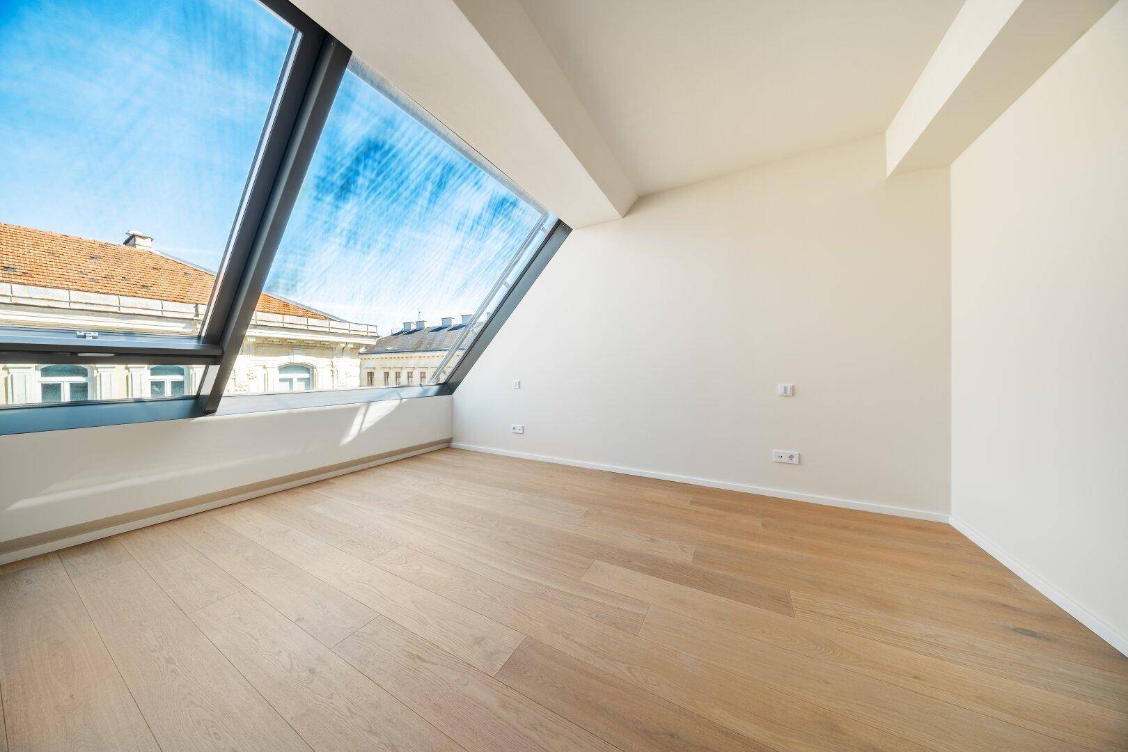 Heller Raum mit Holzboden und schrägem Fenster, das viel natürliches Licht hereinlässt.