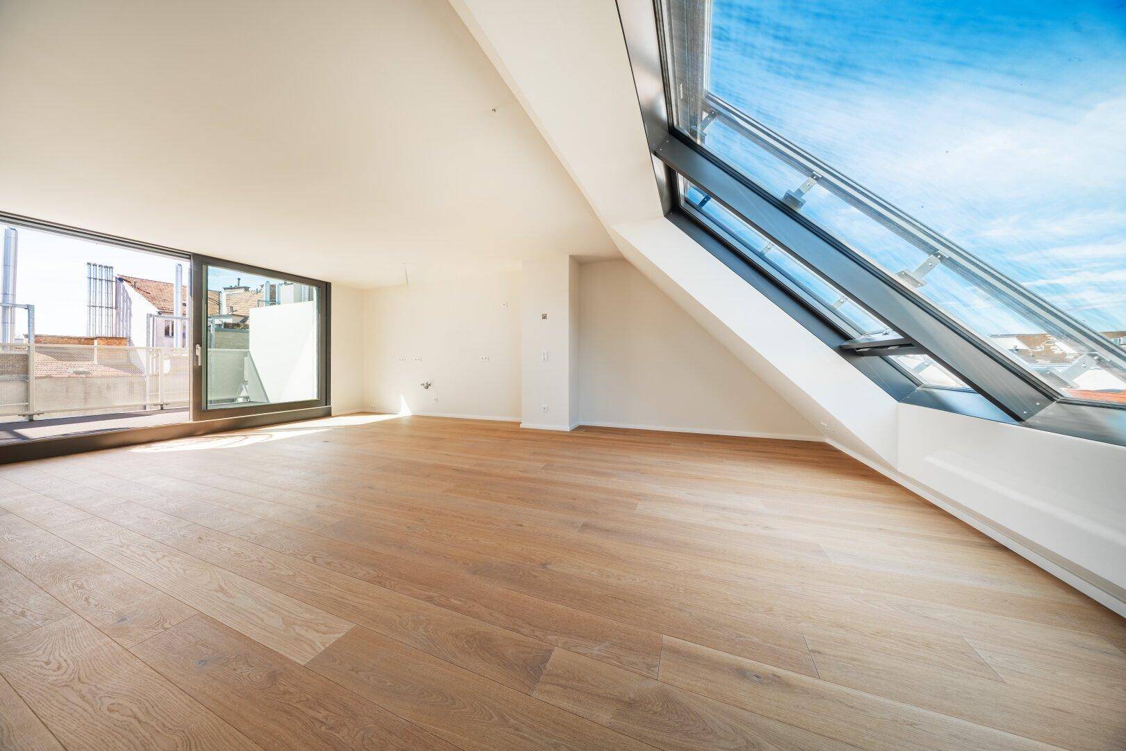 Heller Raum mit Holzboden und Zugang zu einer Terrasse sowie einem großen Dachfenster.