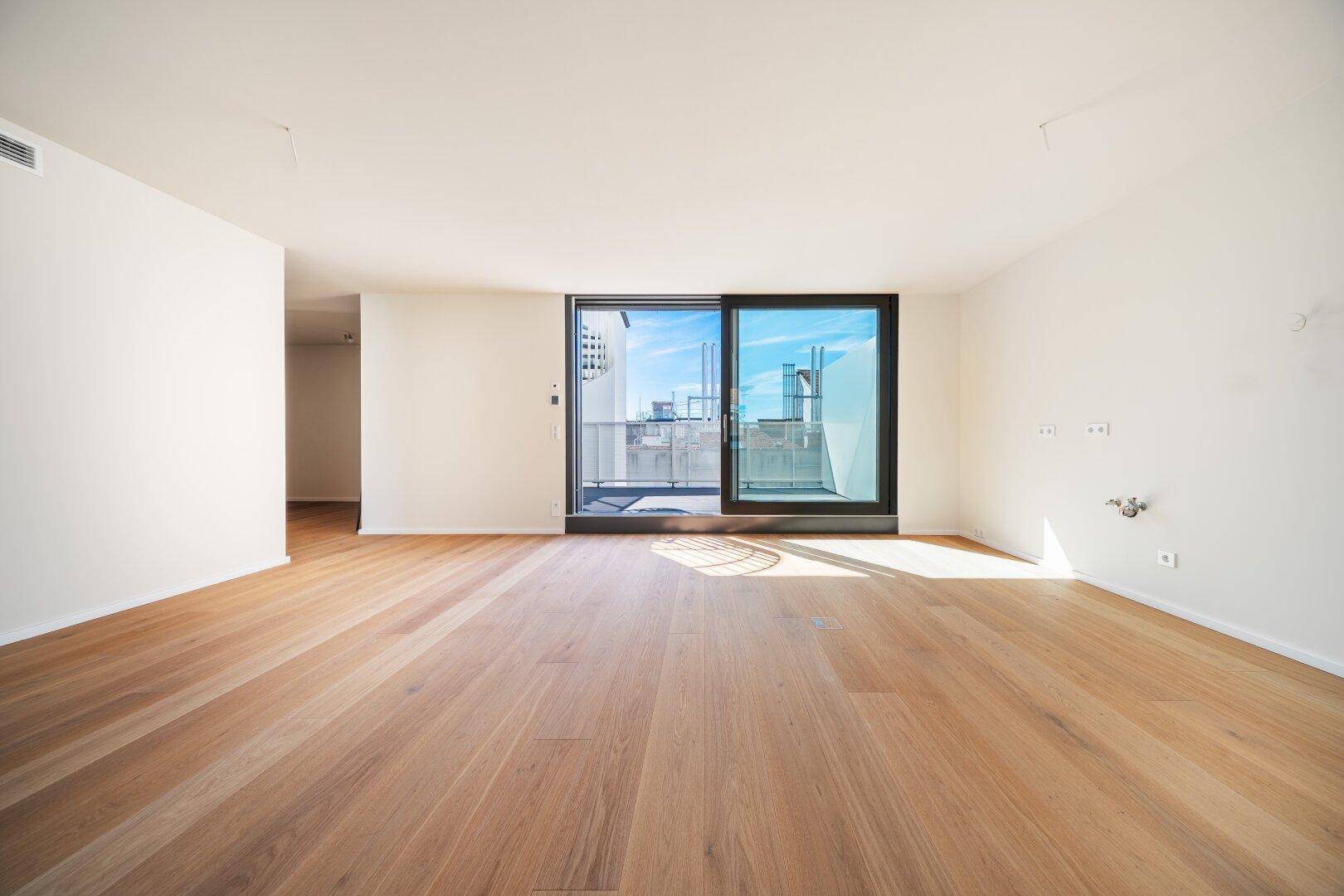 Geräumiger, heller Raum mit Holzboden und Zugang zu einem Balkon oder einer Terrasse.