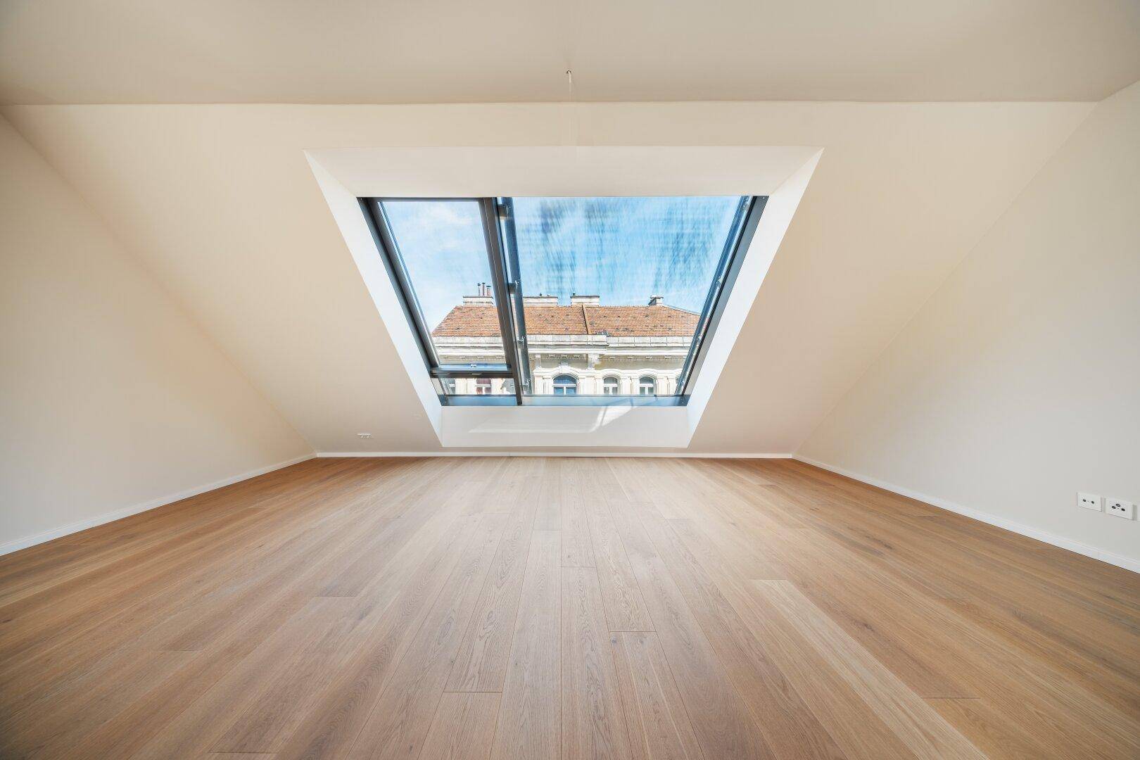 Heller Raum mit Holzboden und einem großen Dachfenster, das viel Tageslicht hereinlässt.
