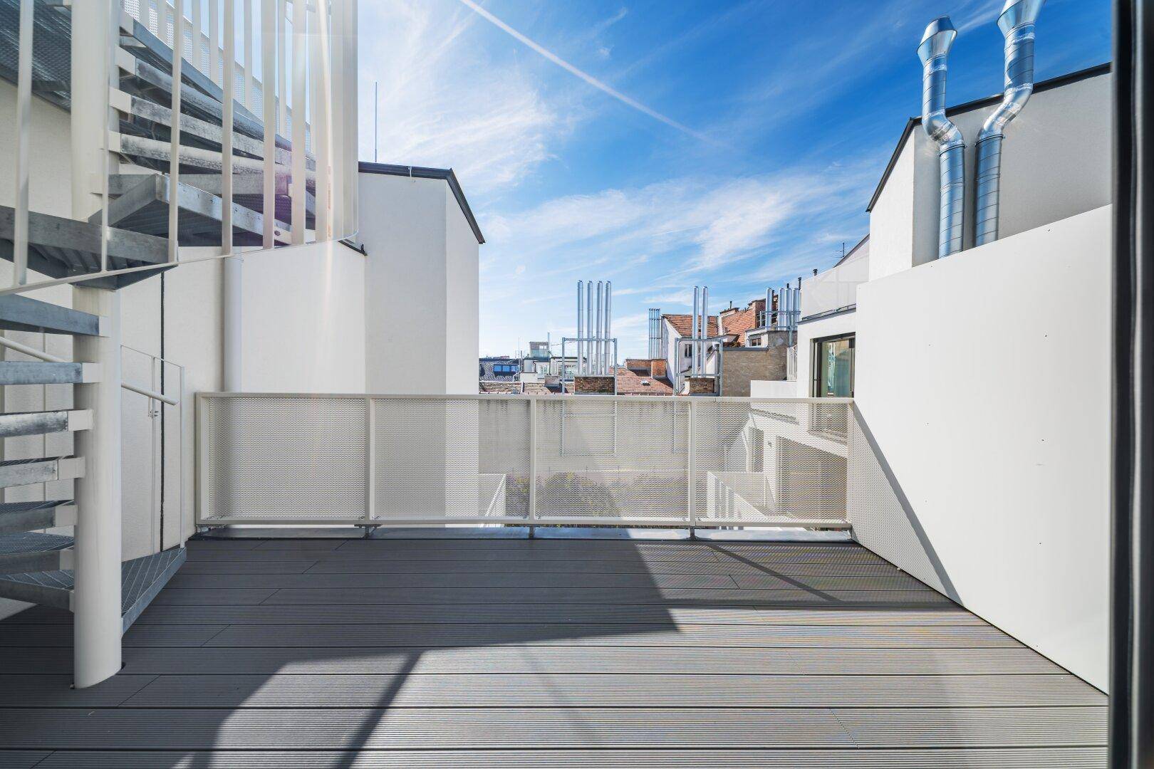 Geräumige Dachterrasse mit Holzbelag und moderner Wendeltreppe unter blauem Himmel.