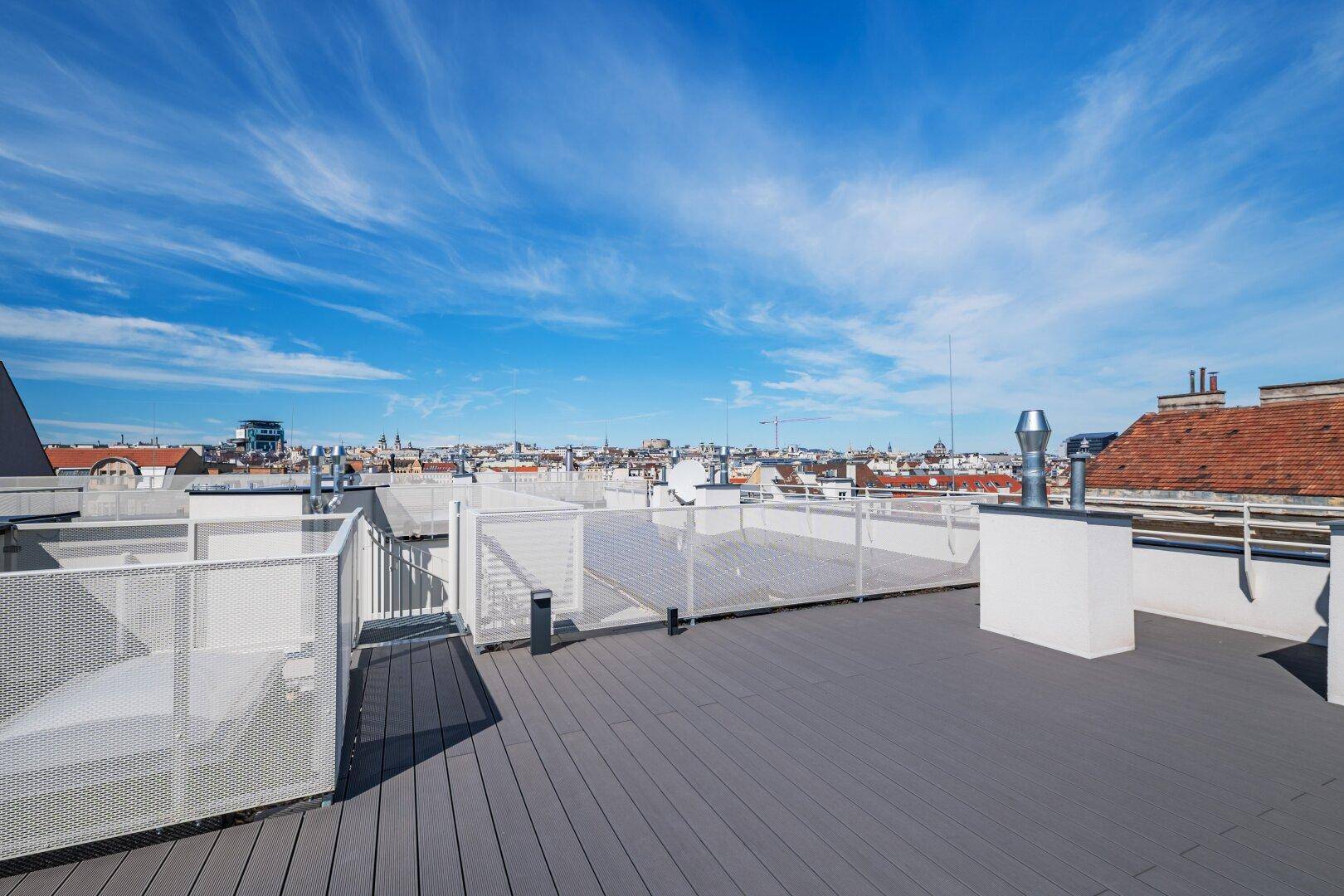 Große Dachterrasse mit weitem Blick über die Dächer der Stadt unter blauem Himmel.