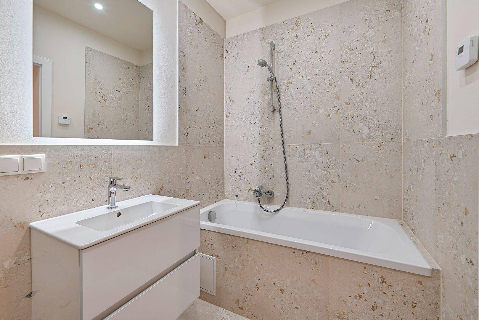 Modernes Badezimmer mit Badewanne, Einzelwaschbecken und beleuchtetem Spiegel.