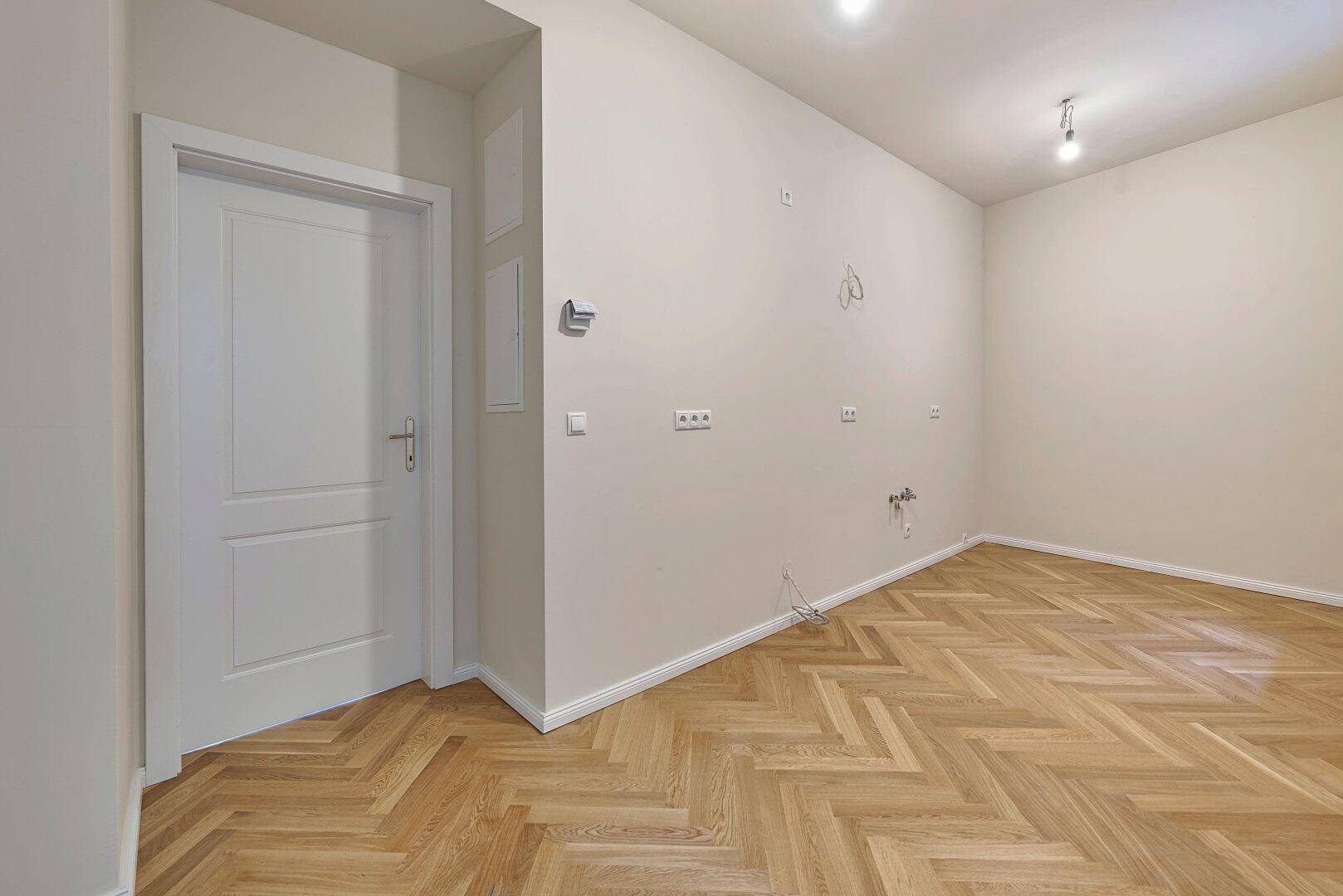 Leerer Raum mit Fischgrätparkett und Tür, bereit für die Installation.