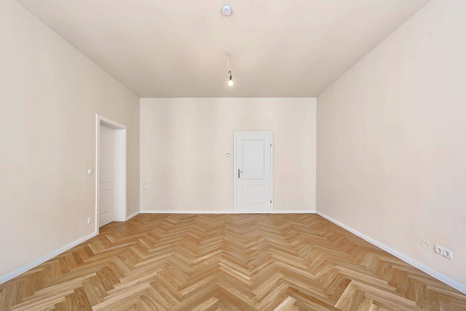 Geräumiges Zimmer mit Fischgrätparkett und zwei Türen, vielseitig nutzbar.