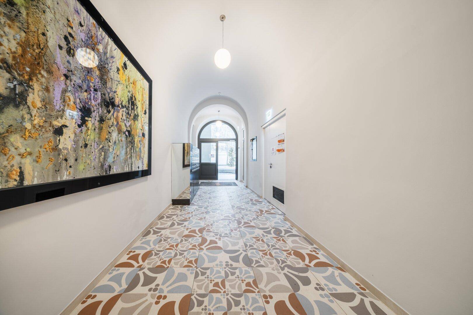Heller Flur mit dekorativem Fliesenboden, Kunstwerk und gewölbter Decke.