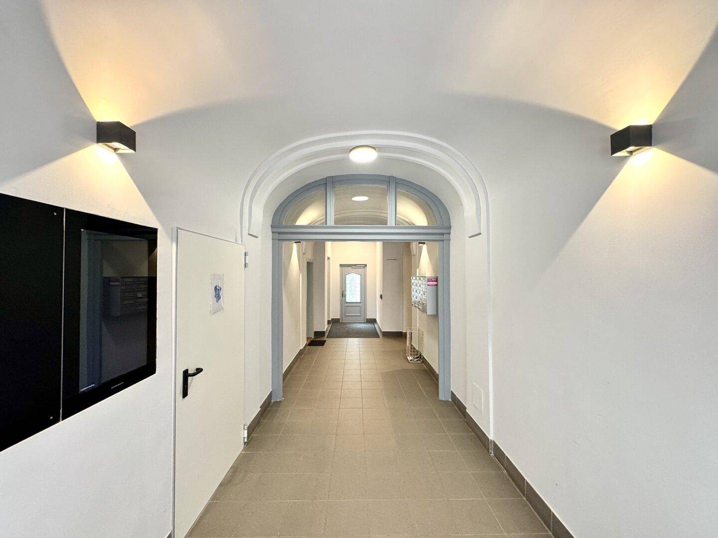 Heller Eingangsbereich des Gebäudes mit gewölbter Decke und Fliesenboden.