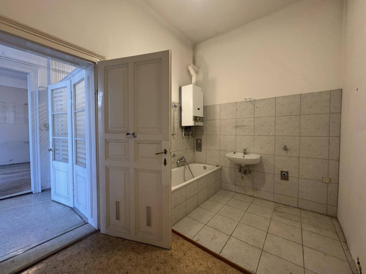 Badezimmer mit Badewanne, Wandfliesen und Blick durch die offene Tür in einen angrenzenden Raum.