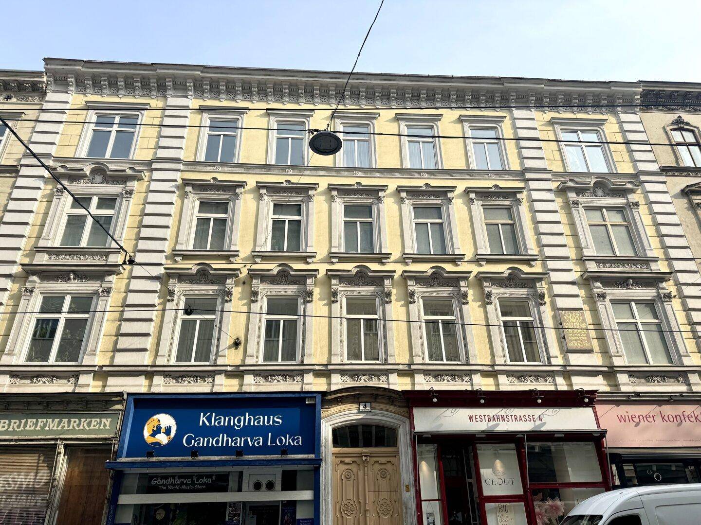 Historische gelbe Fassade eines Altbaus mit vielen Fenstern und Geschäften im Erdgeschoss.