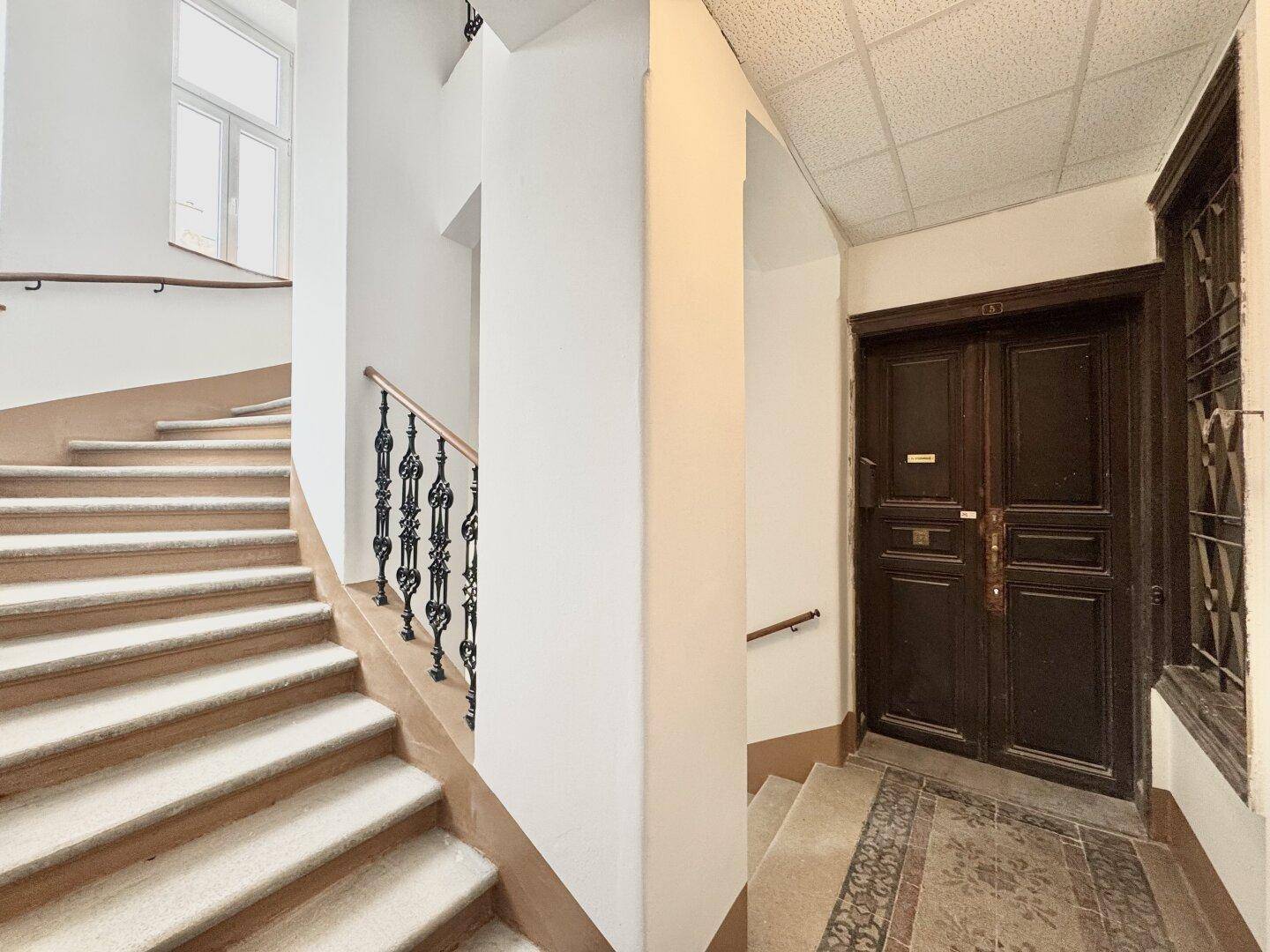 Historisches Treppenhaus mit kunstvollem Geländer und einer großen, dunklen Eingangstür.