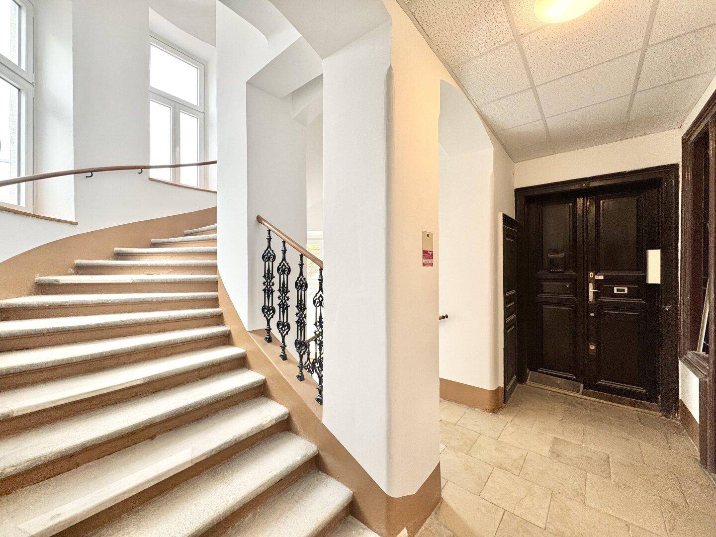 Helles Treppenhaus mit geschwungener Treppe, schmiedeeisernem Geländer und Zugang zu Wohnungen.