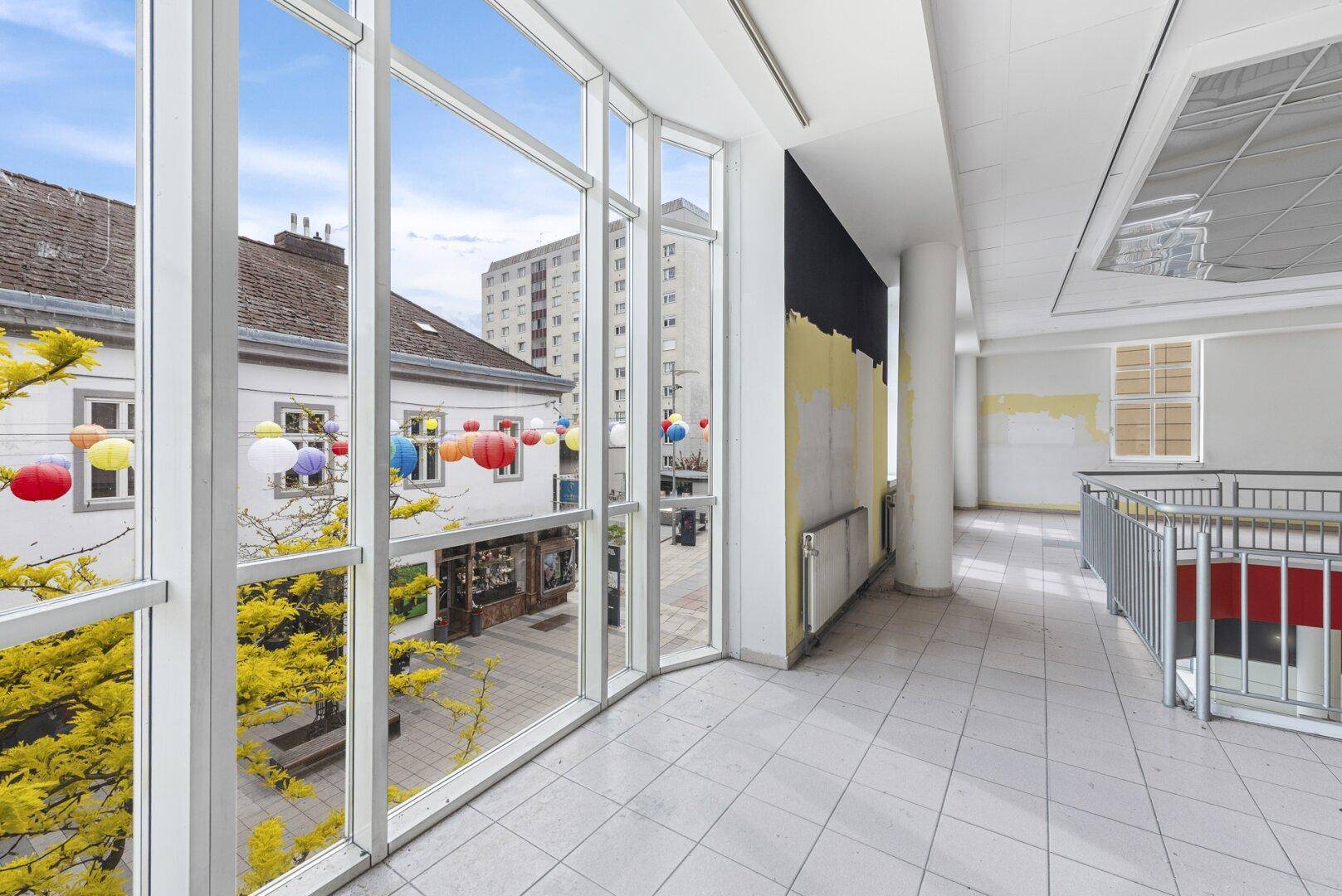 Große Fensterfront mit Blick auf die belebte Fußgängerzone und bunte Dekorationen.