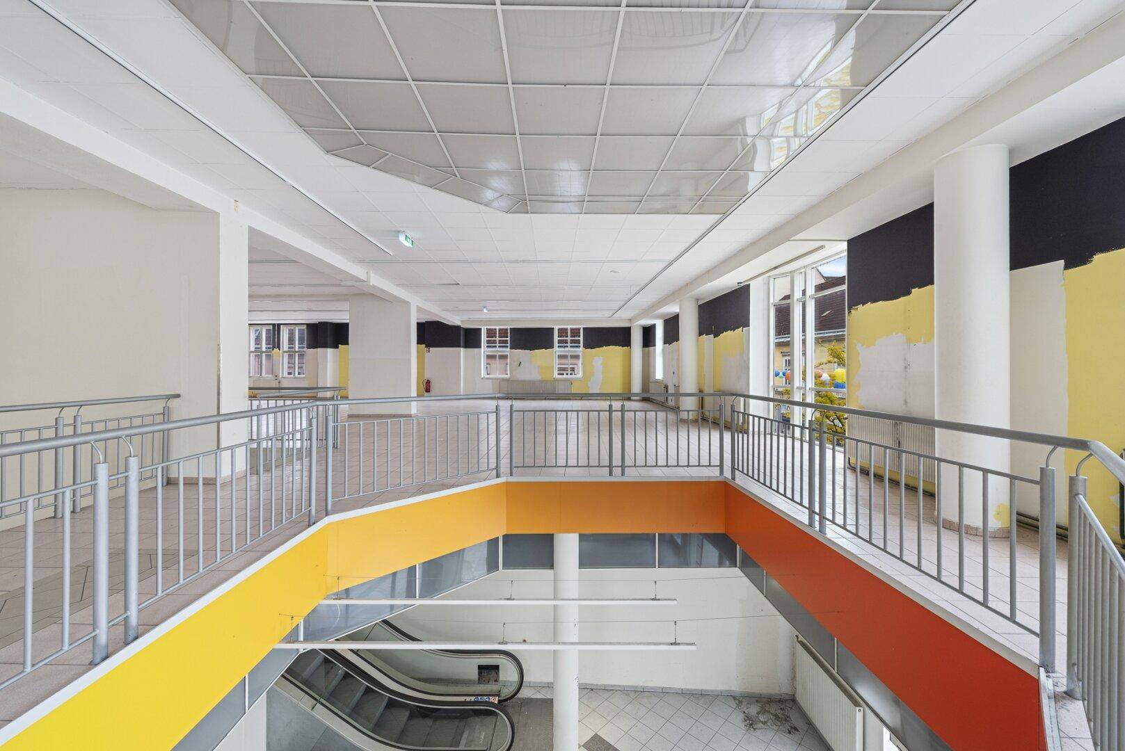 Offene Galerie mit Geländer und Blick auf die Rolltreppe und den unteren Verkaufsbereich.
