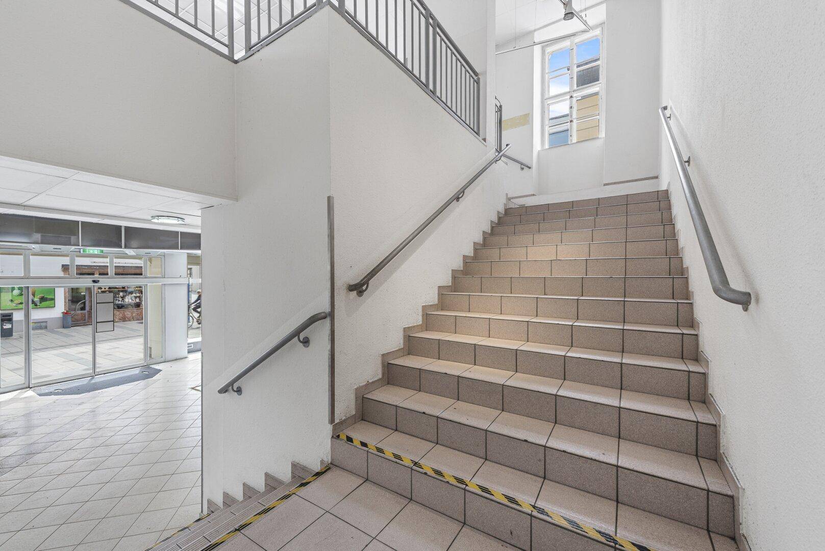 Geräumiges Treppenhaus mit Fliesenboden und Handläufen, bietet Zugang zu verschiedenen Ebenen.