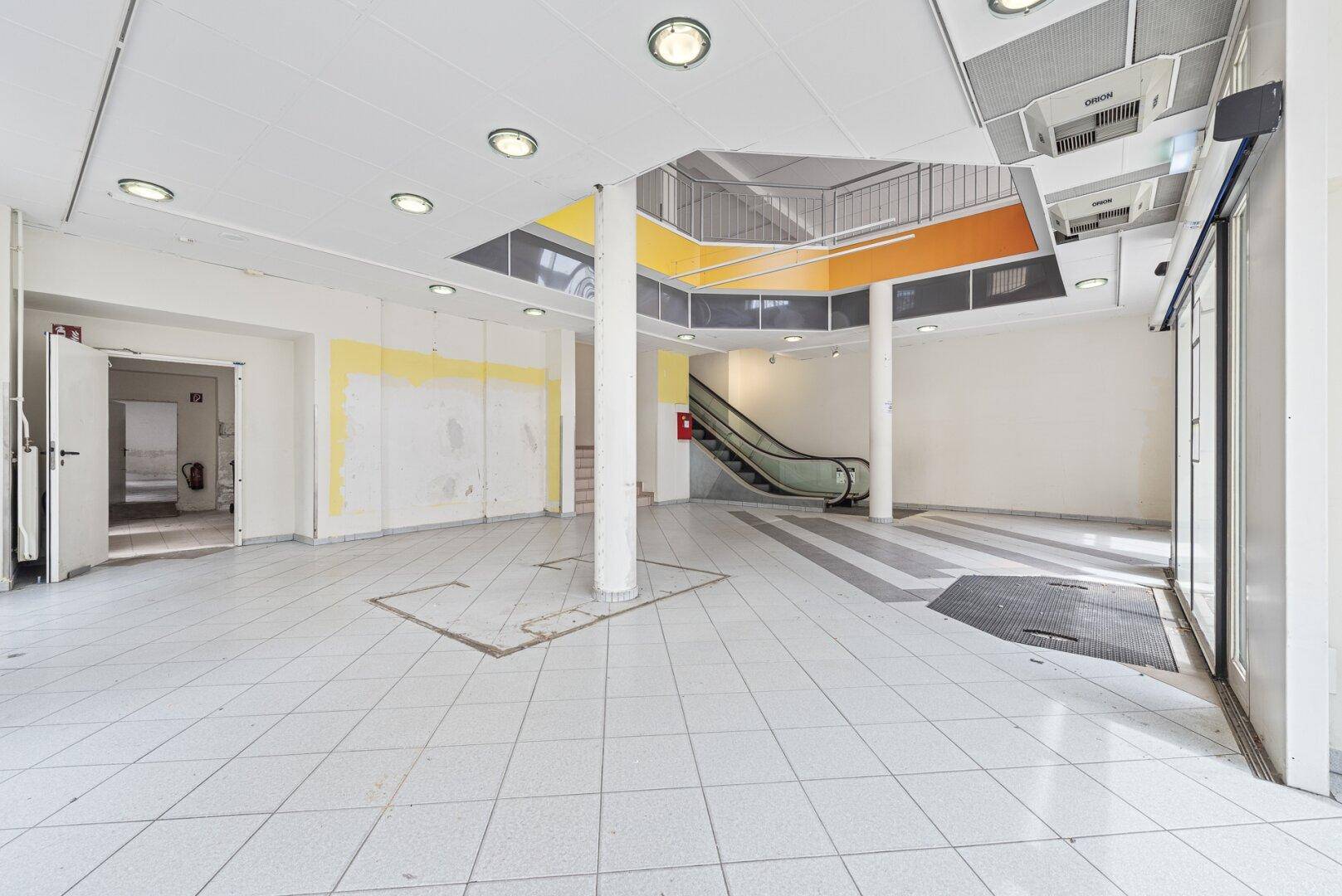 Großer, offener Verkaufsraum mit Fliesenboden, Säulen und Rolltreppe, bereit zur Neugestaltung.