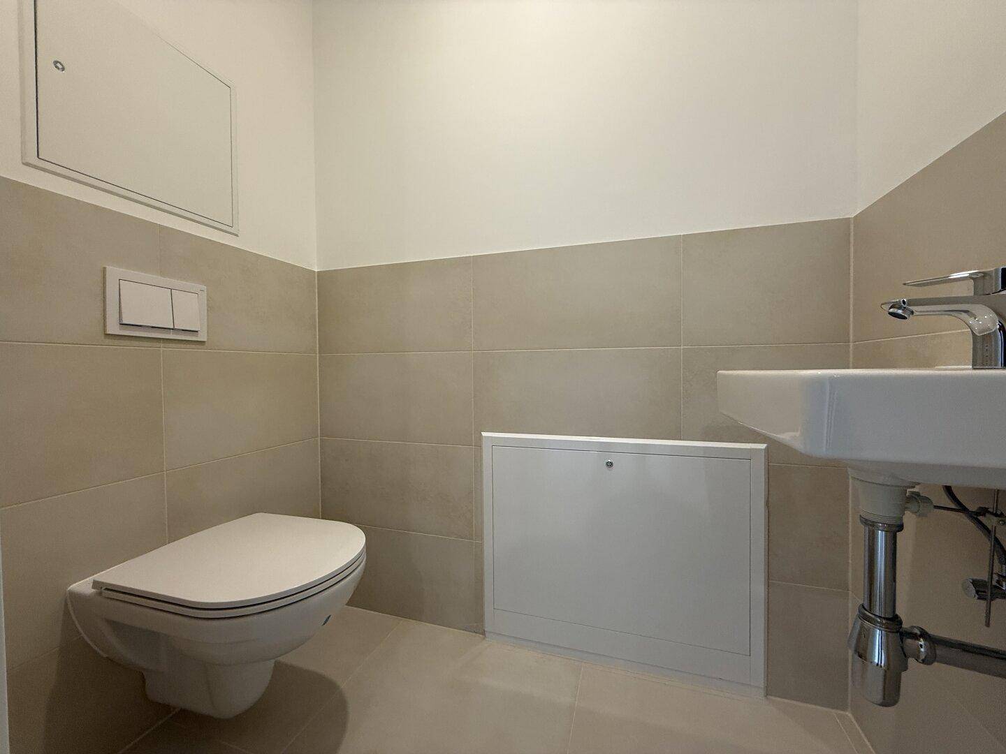 Modernes Gäste-WC mit wandhängender Toilette, Waschbecken und hellen Fliesen.