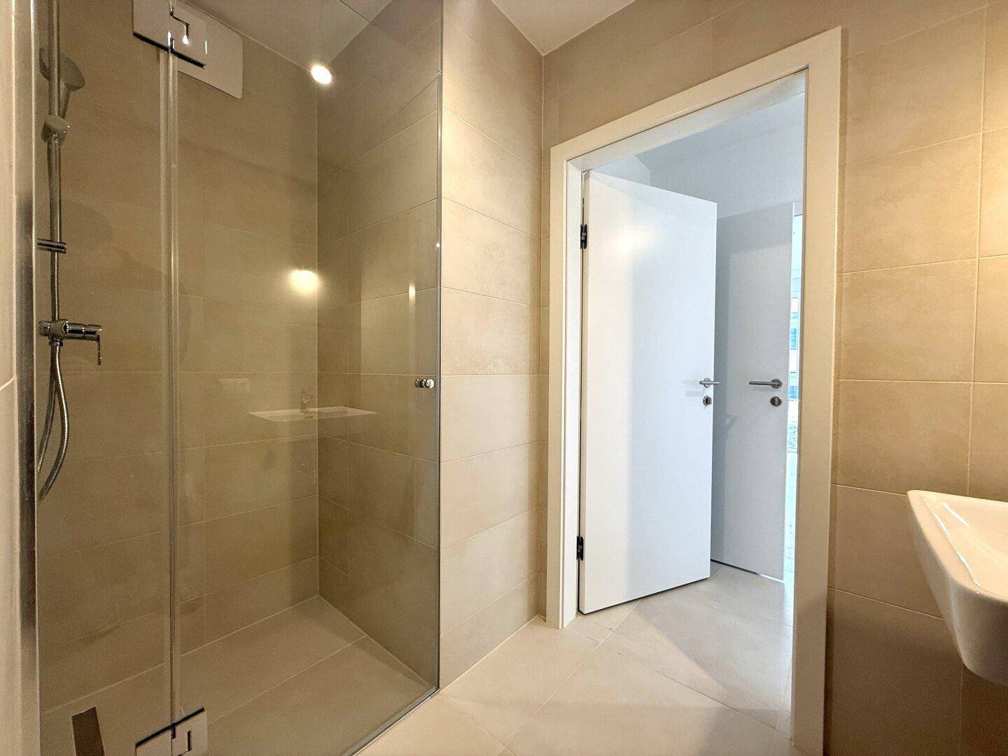 Modernes Badezimmer mit ebenerdiger Dusche, Glasabtrennung und hellem Fliesenboden.