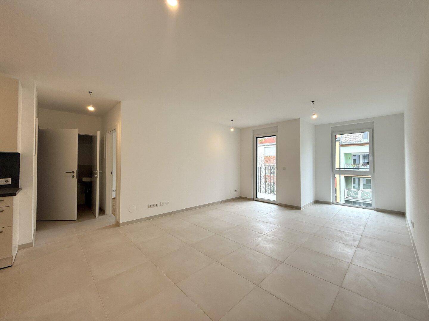 Heller Wohnbereich mit Fliesenboden, weißen Wänden und Zugang zu einem Balkon.