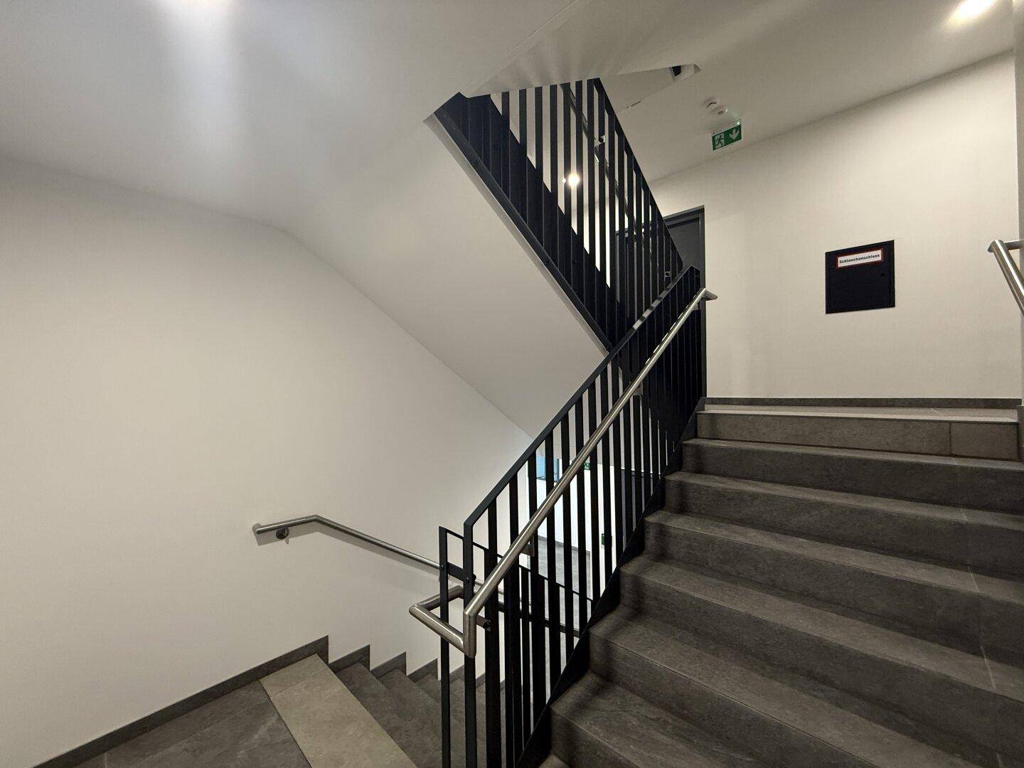 Modernes Treppenhaus mit dunklen Stufen und Metallgeländer in einem Mehrfamilienhaus.