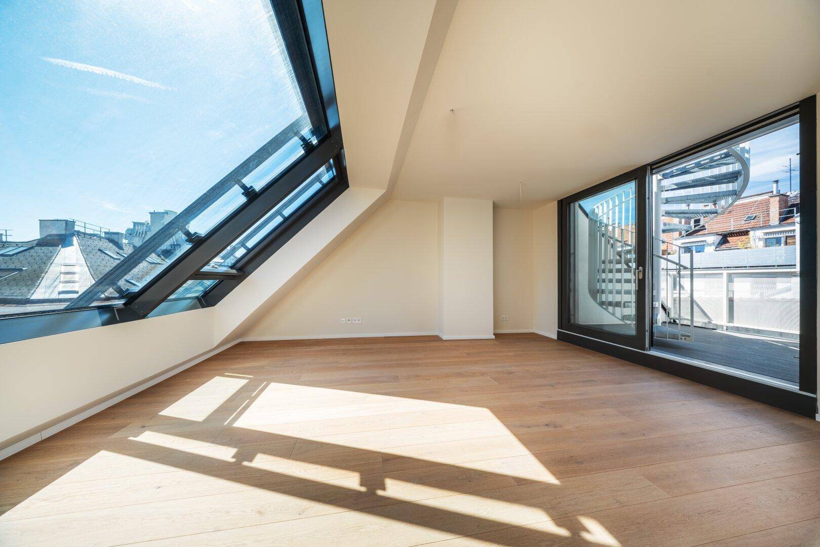 Lichtdurchfluteter Raum mit großen Dachfenstern, Holzboden und Wendeltreppe zum Außenbereich.