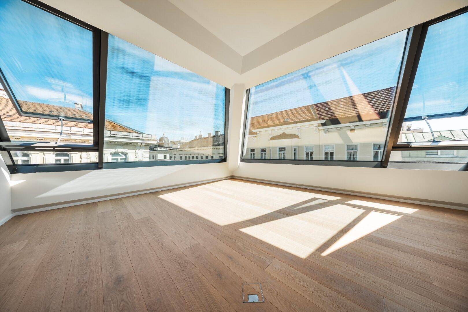 Heller Eckraum mit großen Schrägfenstern und weitem Blick über die Dächer der Stadt.