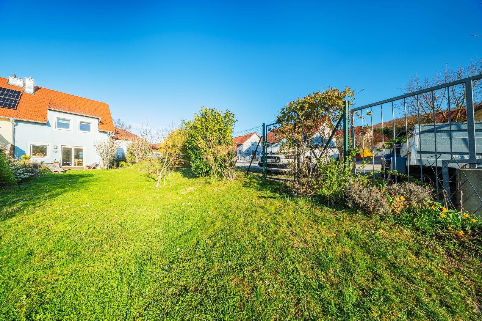 Gartenbereich hinter dem Haus mit Photovoltaikanlage auf dem Dach und grüner Wiese.