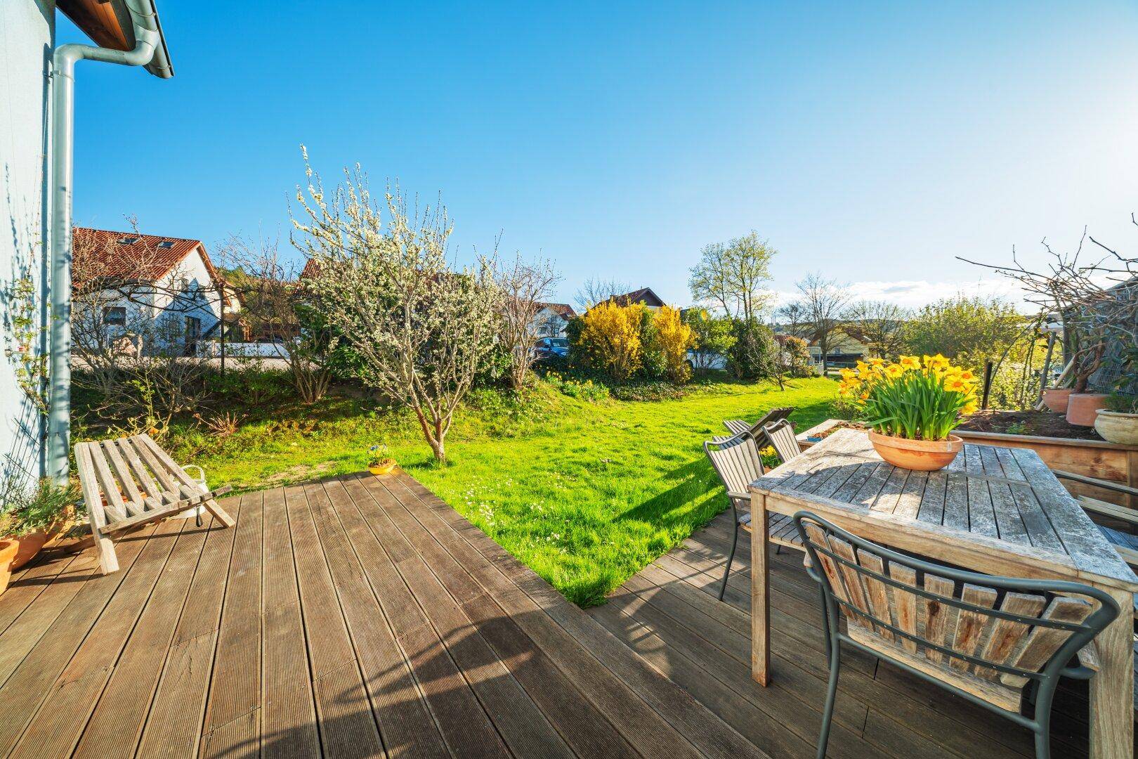 Sonnige Holzterrasse mit Gartenmöbeln und Blick auf den weitläufigen Garten.