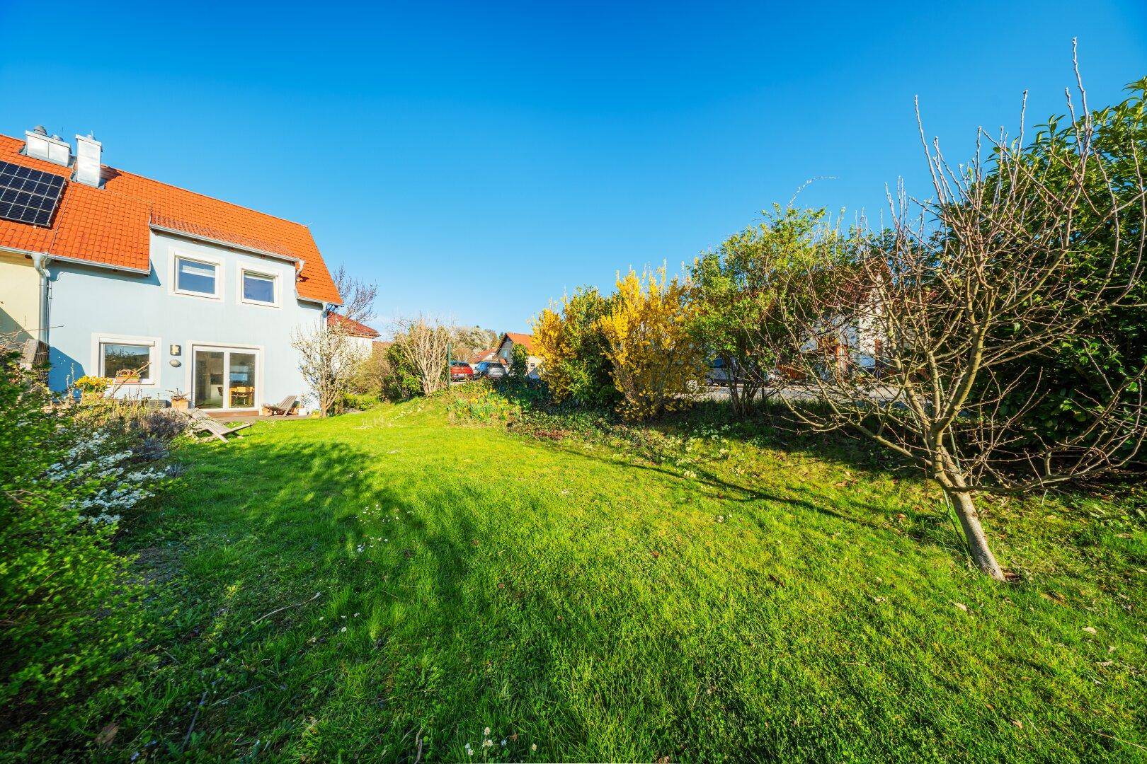 Großer grüner Garten mit Rasenfläche und Blick auf die Rückseite des Hauses mit Solaranlage.