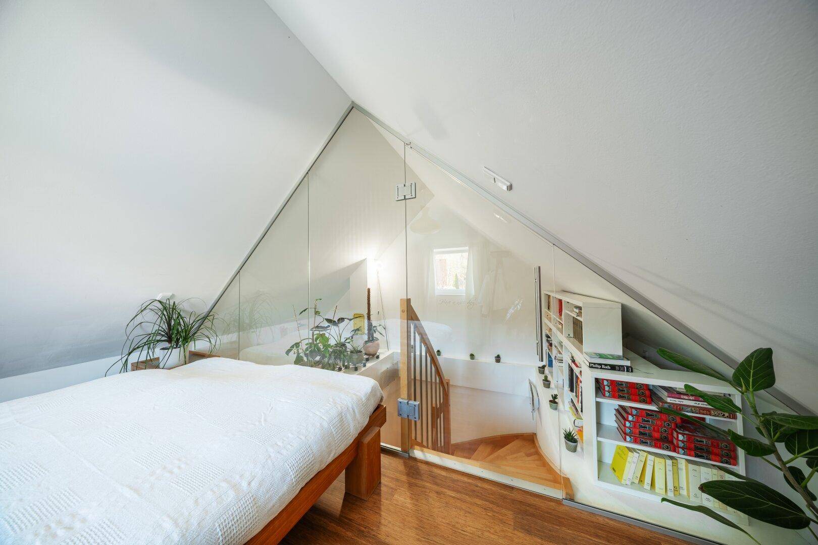 Schlafzimmer im Dachgeschoss mit Glasabtrennung und Blick auf die Treppe.