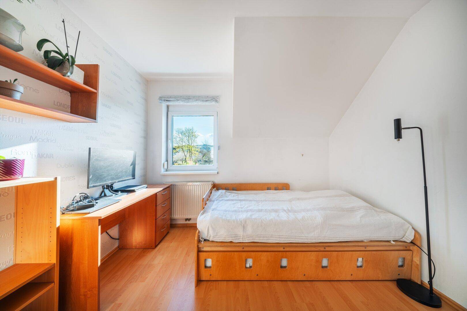 Schlafzimmer mit Holzboden, Schreibtisch und Fenster im Dachgeschoss.