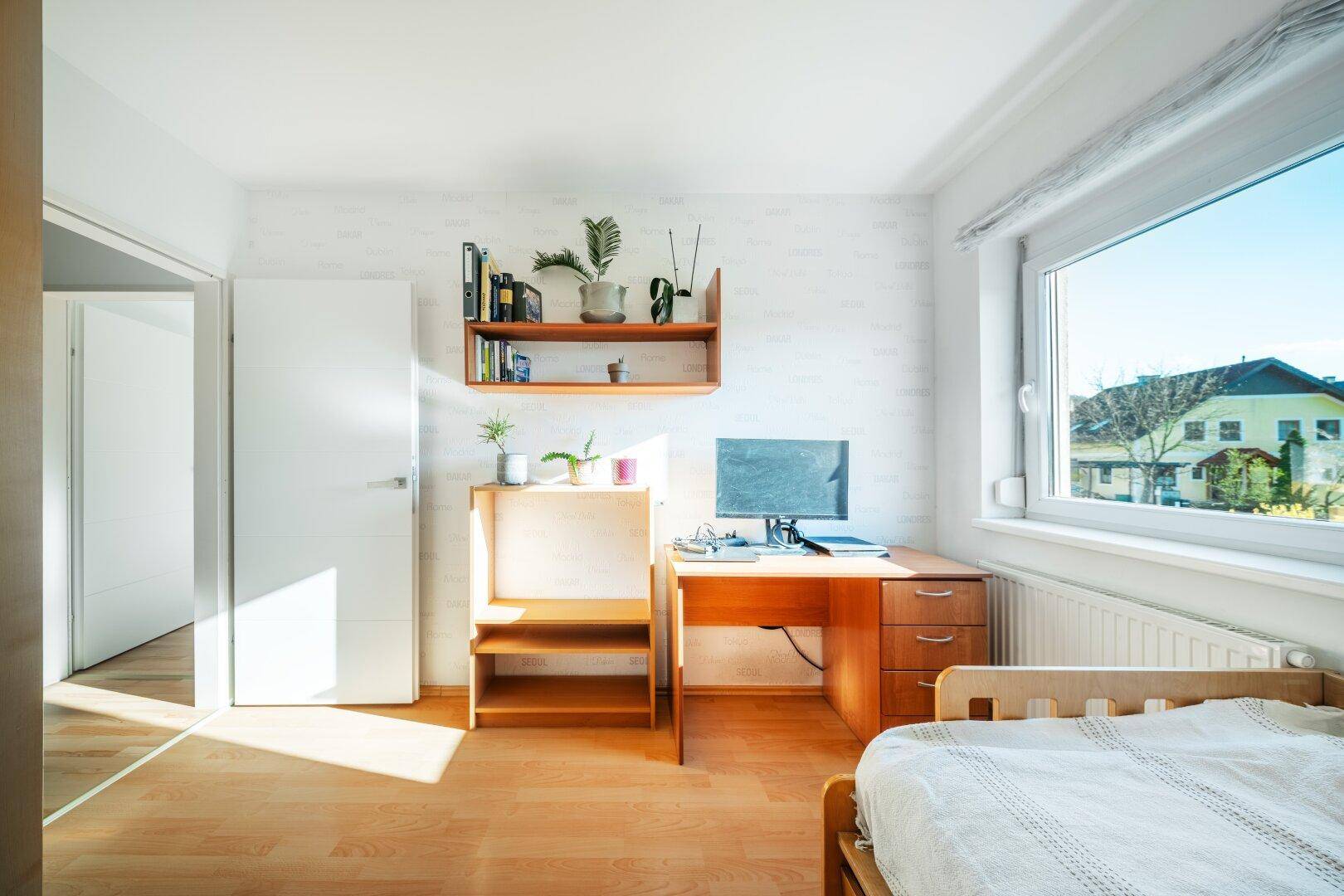 Helles Schlafzimmer mit Holzboden, Schreibtisch und großem Fenster.
