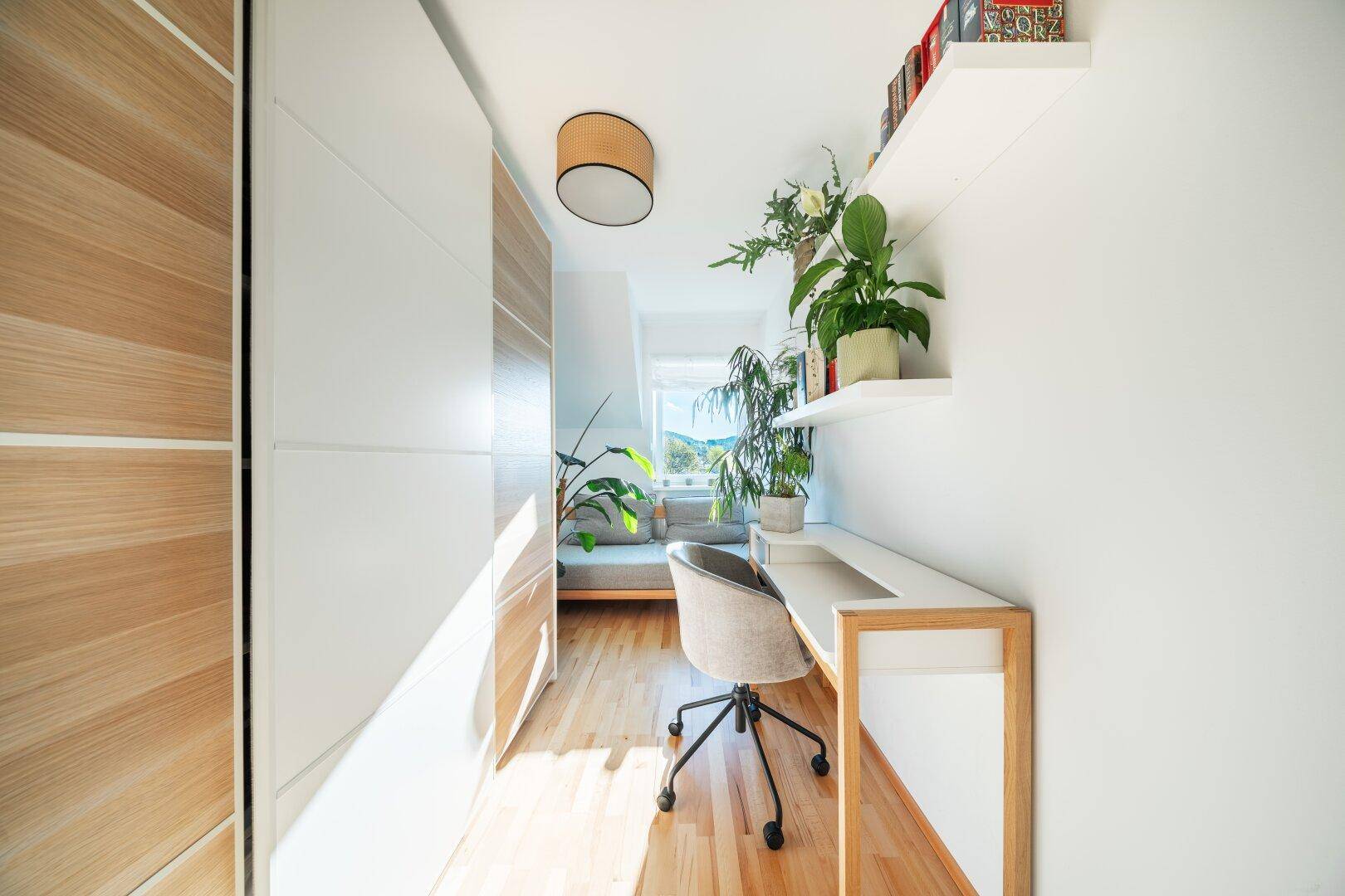 Helles Arbeitszimmer mit Holzboden, Einbauschränken und Fenster im Dachgeschoss.