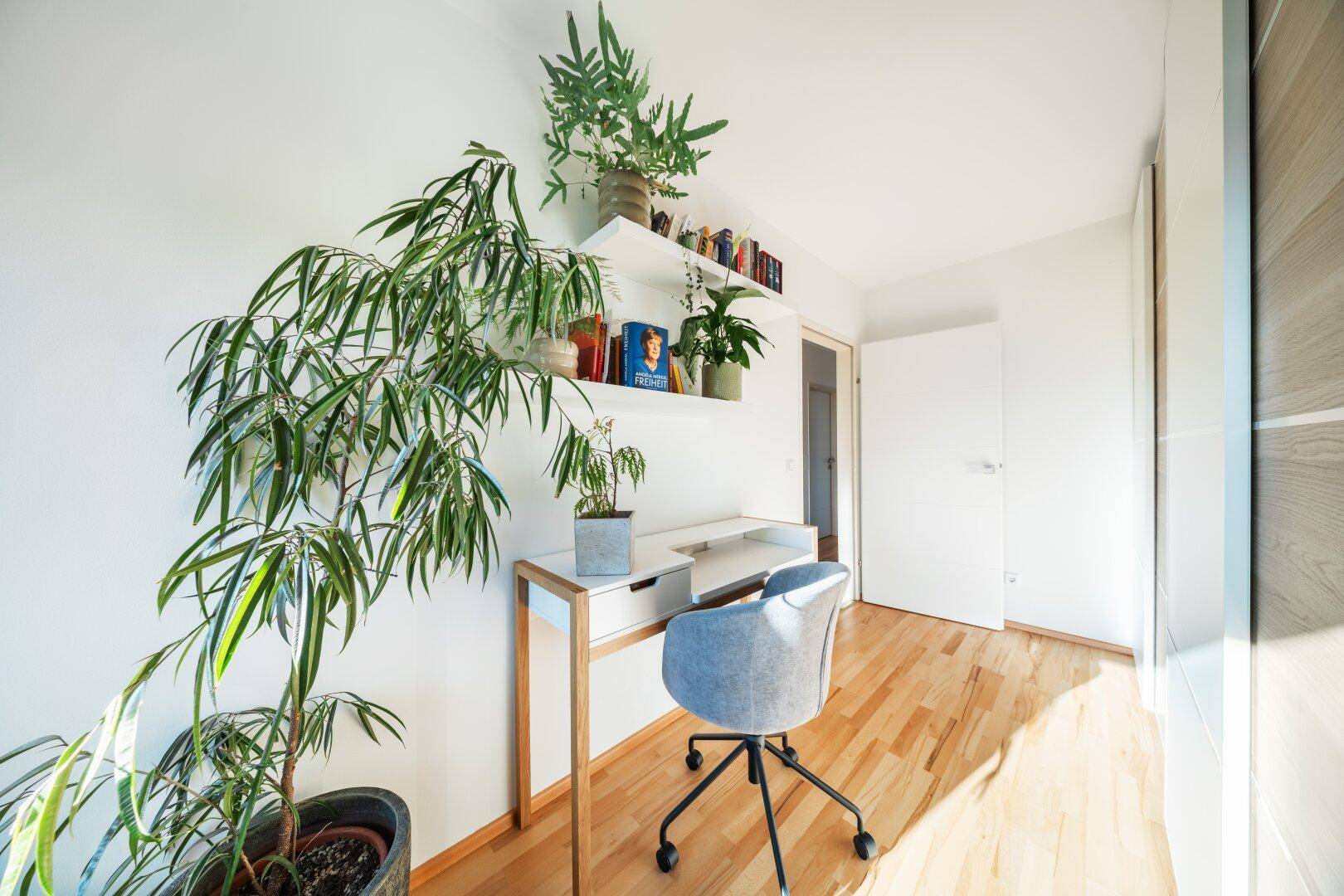 Modernes Arbeitszimmer mit Holzboden, Schreibtisch und Pflanzen auf Regalen.