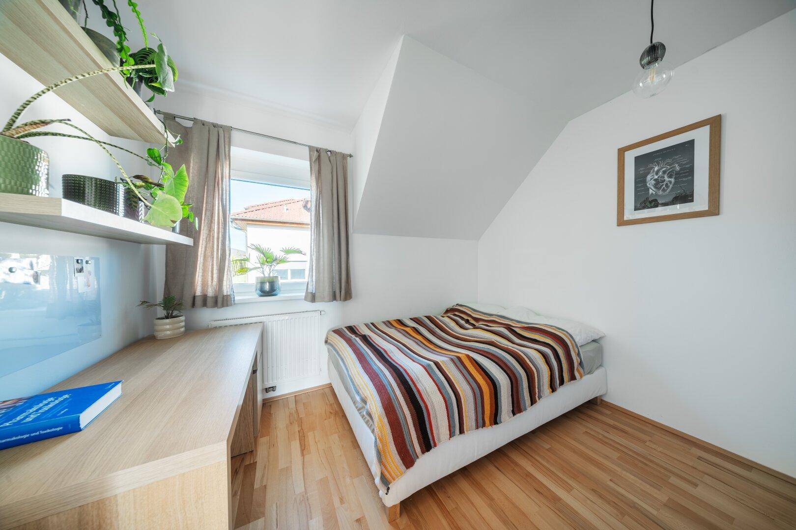 Gemütliches Schlafzimmer im Dachgeschoss mit Holzboden und Schreibtisch.
