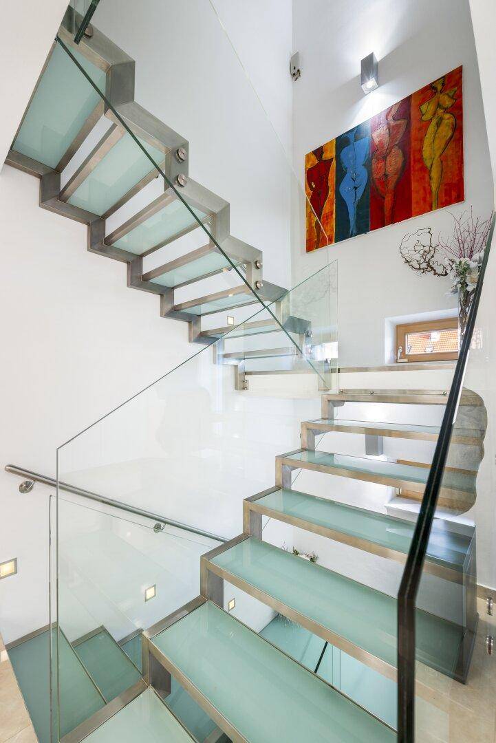 Moderne Treppe mit Glasgeländer und schwebenden Stufen, beleuchtet von oben.