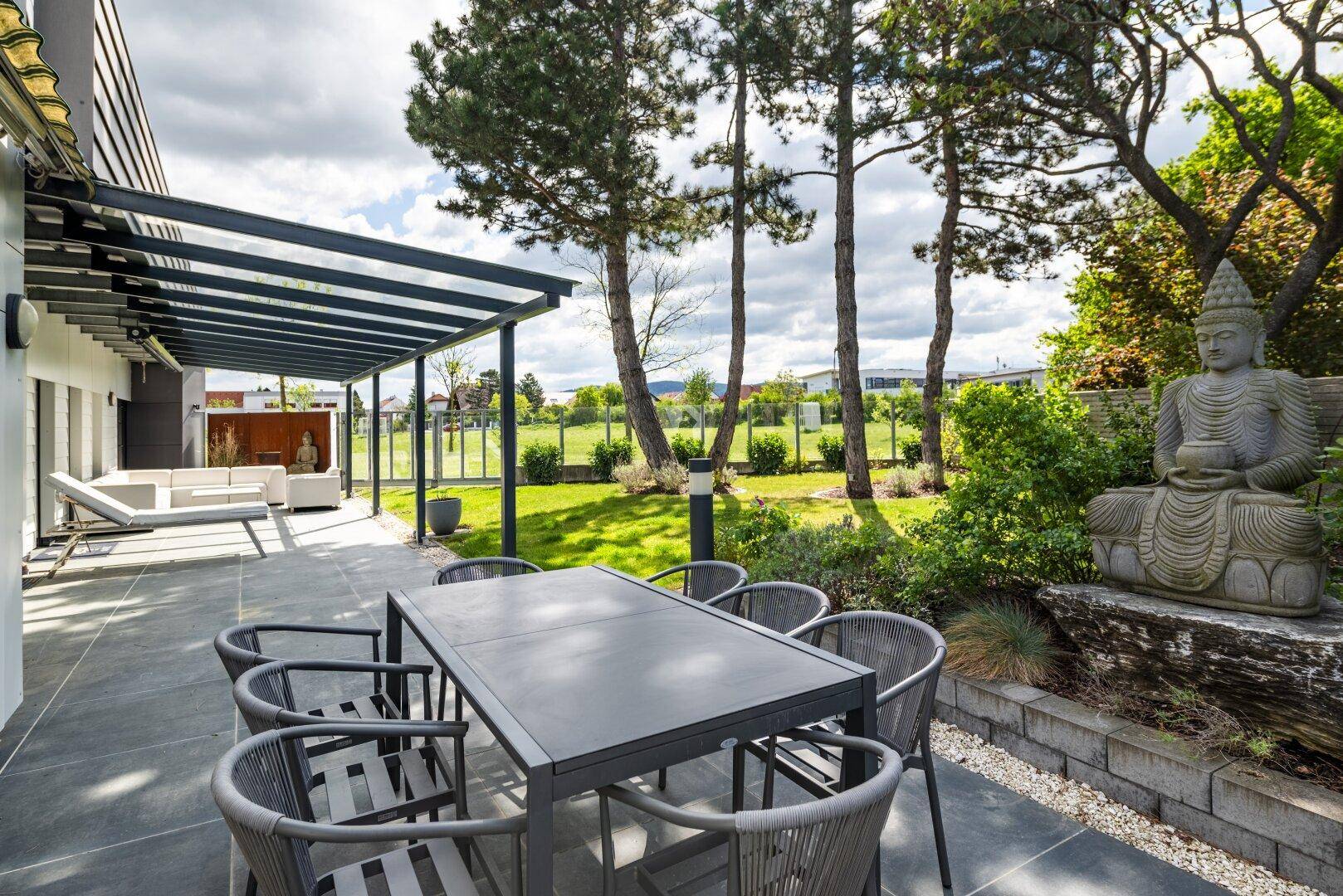 Großzügige Terrasse mit modernen Gartenmöbeln, Überdachung und Blick ins Grüne.
