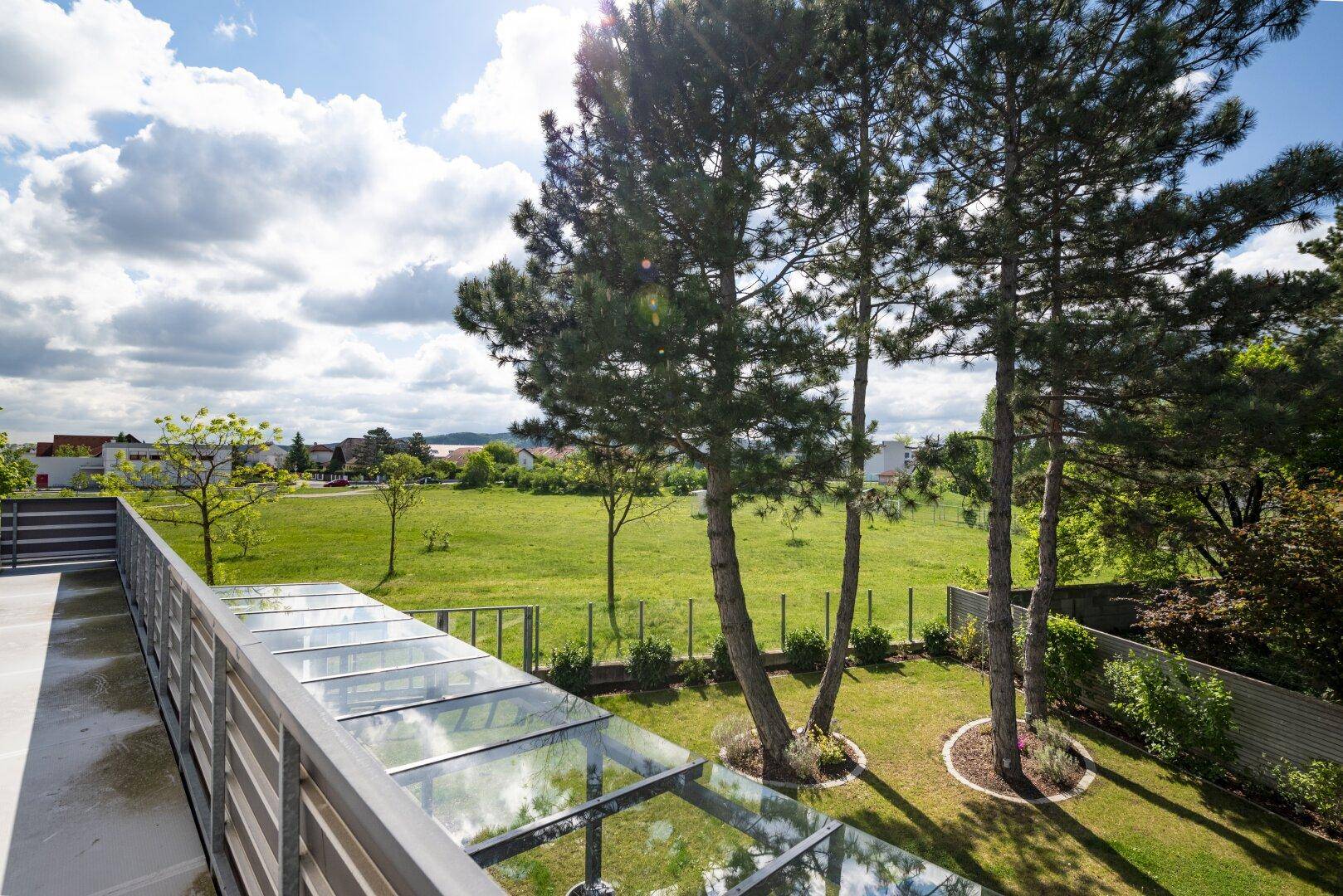 Großer Balkon mit weitem Blick über grüne Felder und Bäume.