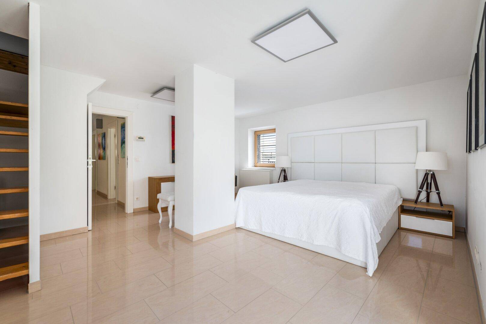 Geräumiges Schlafzimmer mit großem weißen Bett, Fliesenboden und einem Fenster für Tageslicht.