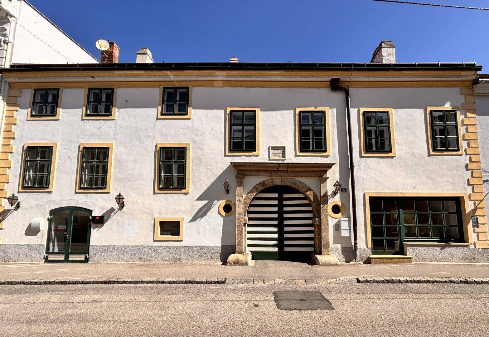 Historische Gebäudefassade mit vielen Fenstern und einem großen, bogenförmigen Eingangstor zur Straße hin.