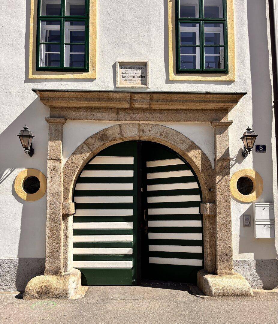 Detailansicht des großen, bogenförmigen Eingangstors mit historischen Laternen und einer Inschriftentafel.