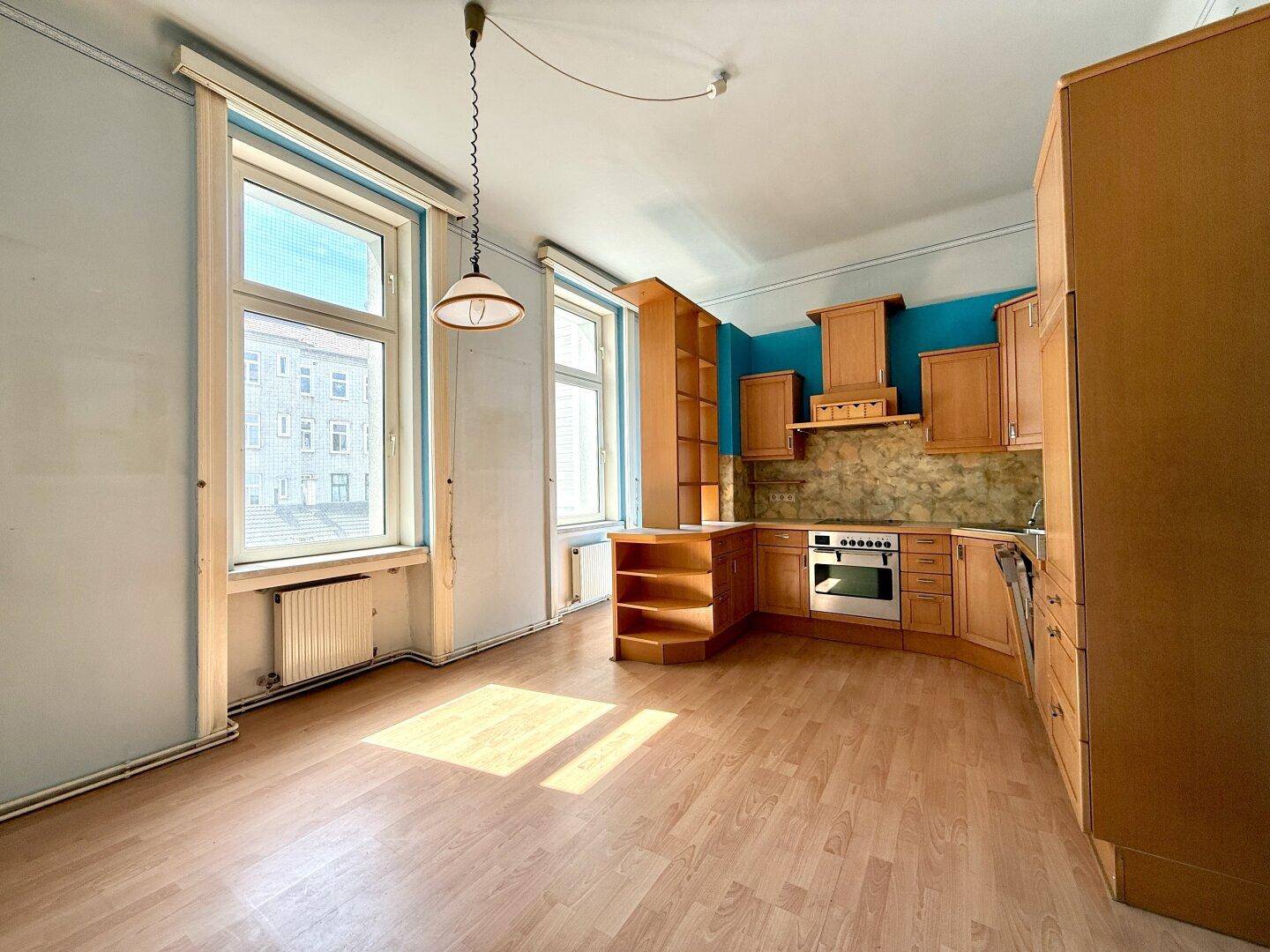 Geräumige Küche mit Holzschränken, blauer Wandfarbe und zwei großen Fenstern.