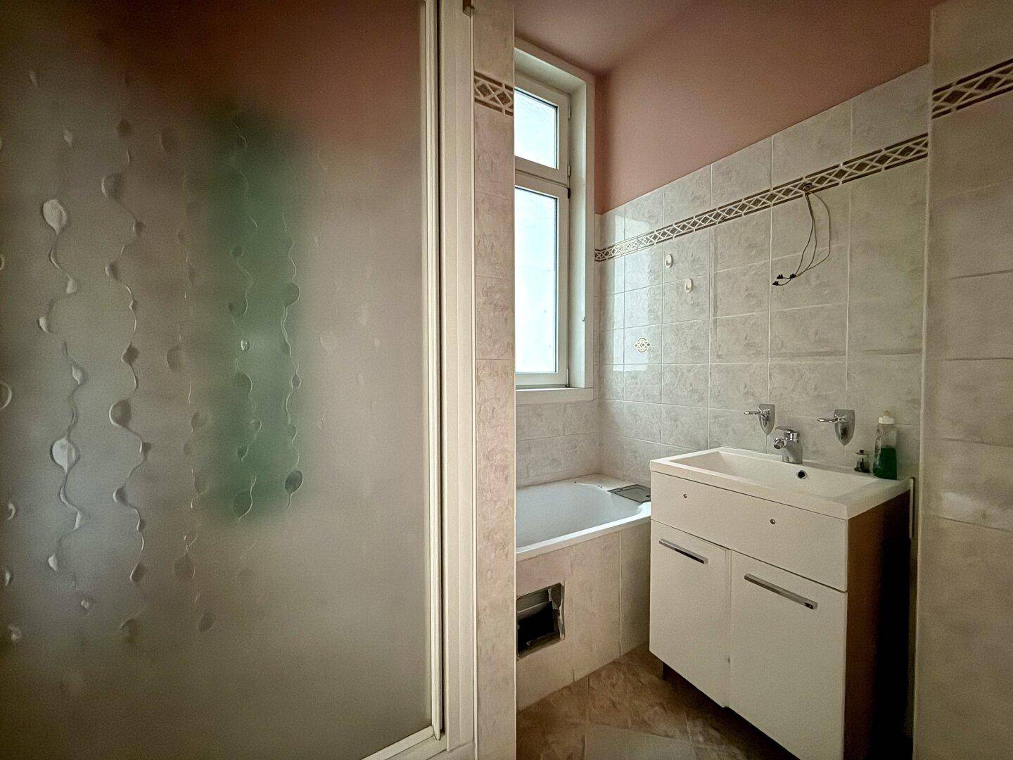 Badezimmer mit Badewanne, Duschkabine, Waschbecken und einem Fenster für Tageslicht.
