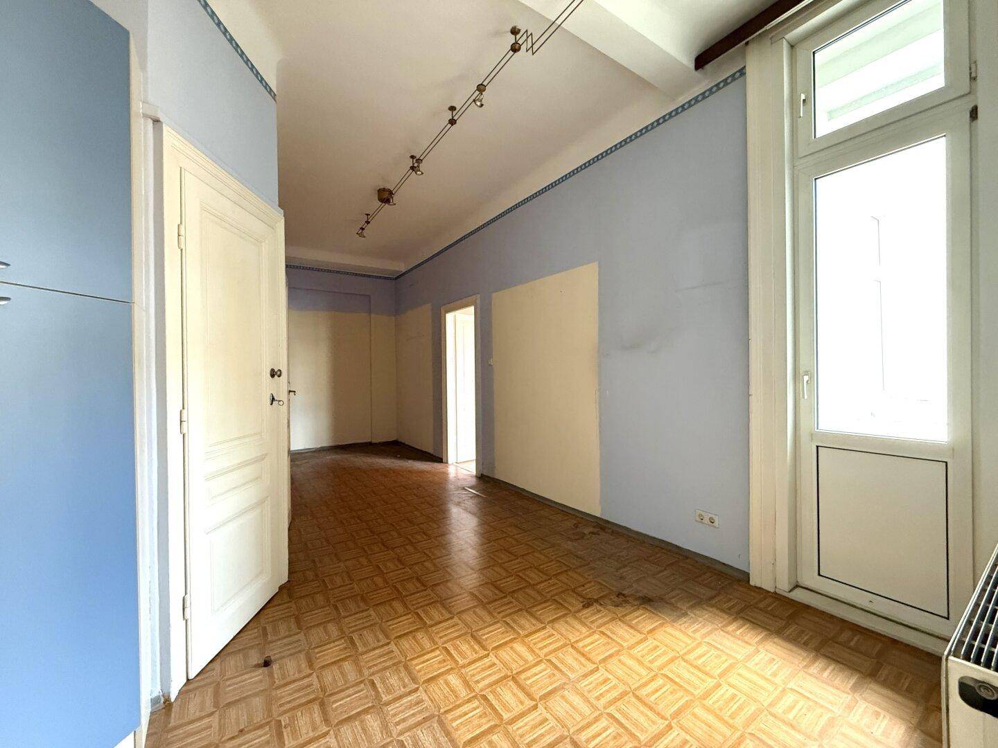 Heller Flur mit Holzboden, blauen Wänden und Zugang zu einem Balkon oder einer Loggia.