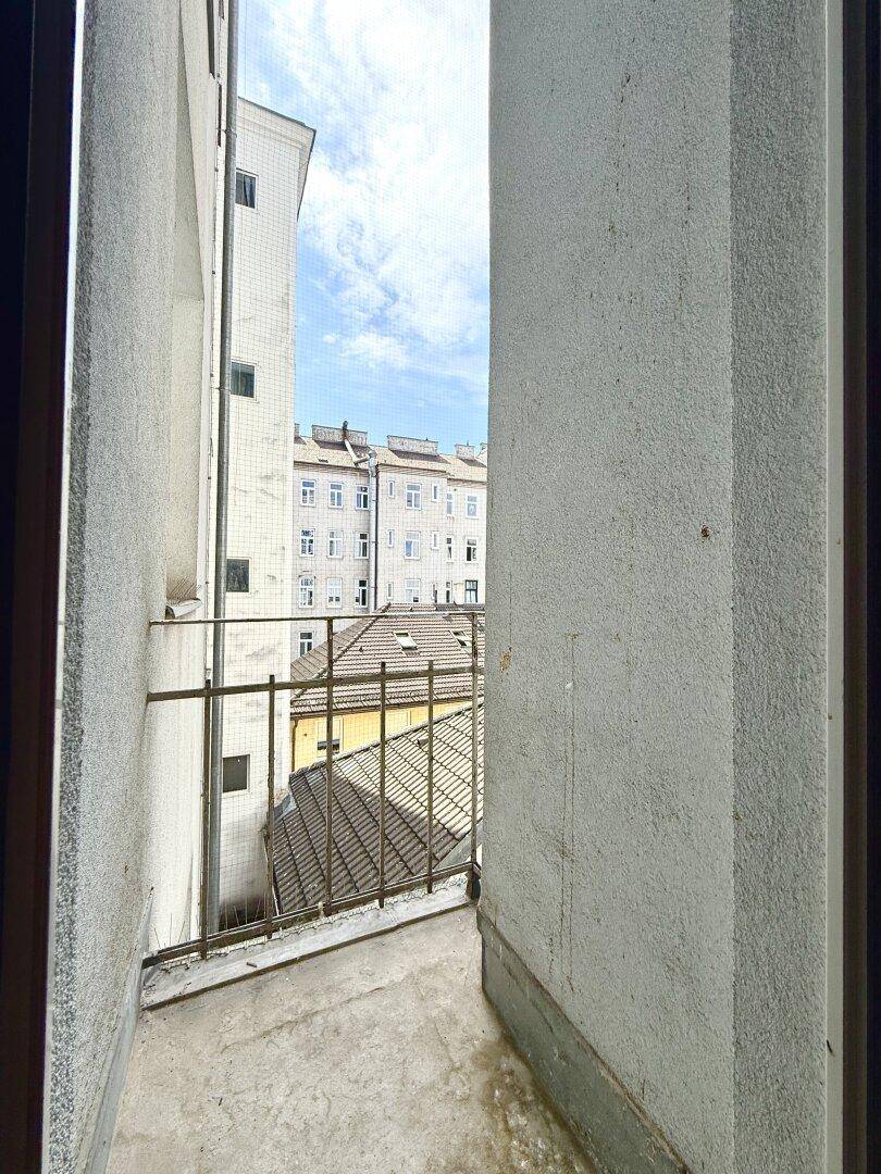 Schmaler Balkon mit Metallgeländer und Blick auf umliegende Gebäude und Dächer.
