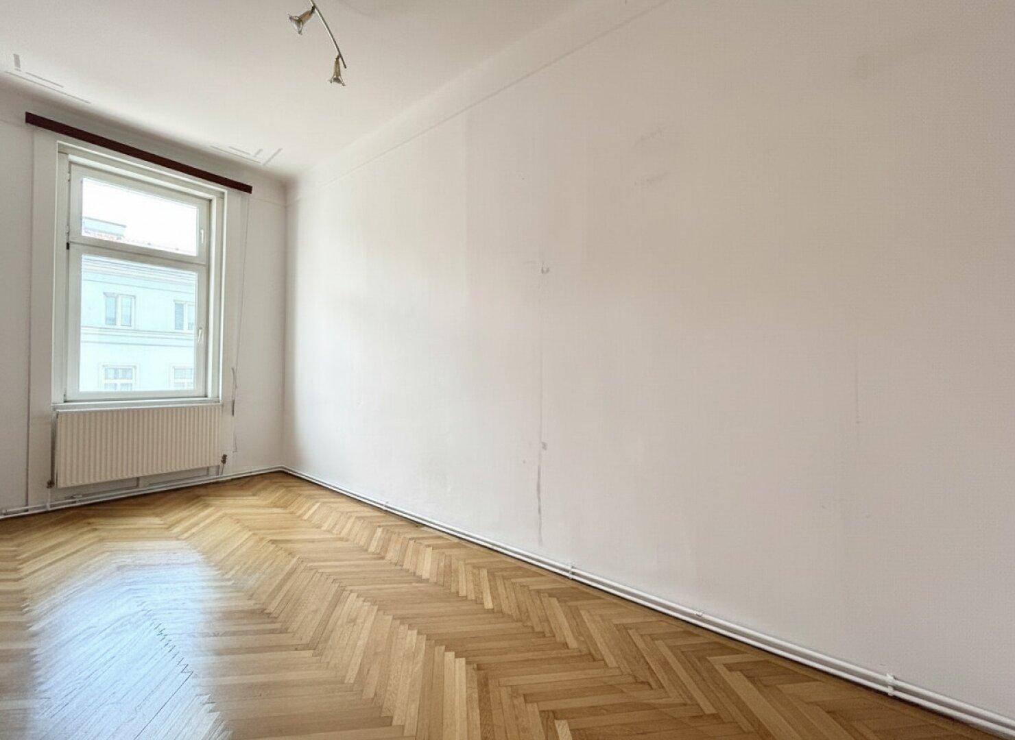 Helles, leeres Zimmer mit frisch gestrichenen weißen Wänden und Fischgrätparkettboden.