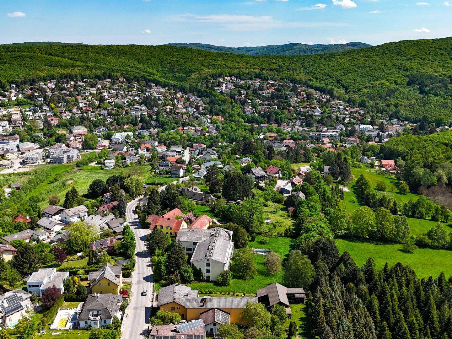 Panoramablick auf eine malerische Stadt, eingebettet in grüne Hügel und Wälder unter blauem Himmel.