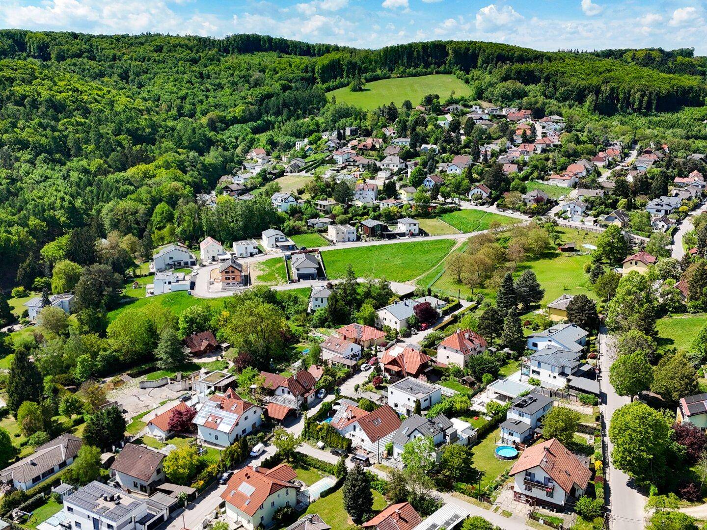 Weitläufige Luftaufnahme einer Wohnsiedlung mit vielen Häusern und grünen Hügeln im Hintergrund.