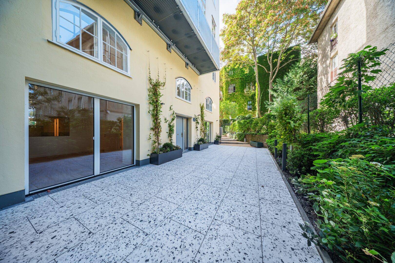 Moderne Terrasse im Erdgeschoss mit großen Glasschiebetüren und Zugang zu einem begrünten Außenbereich.
