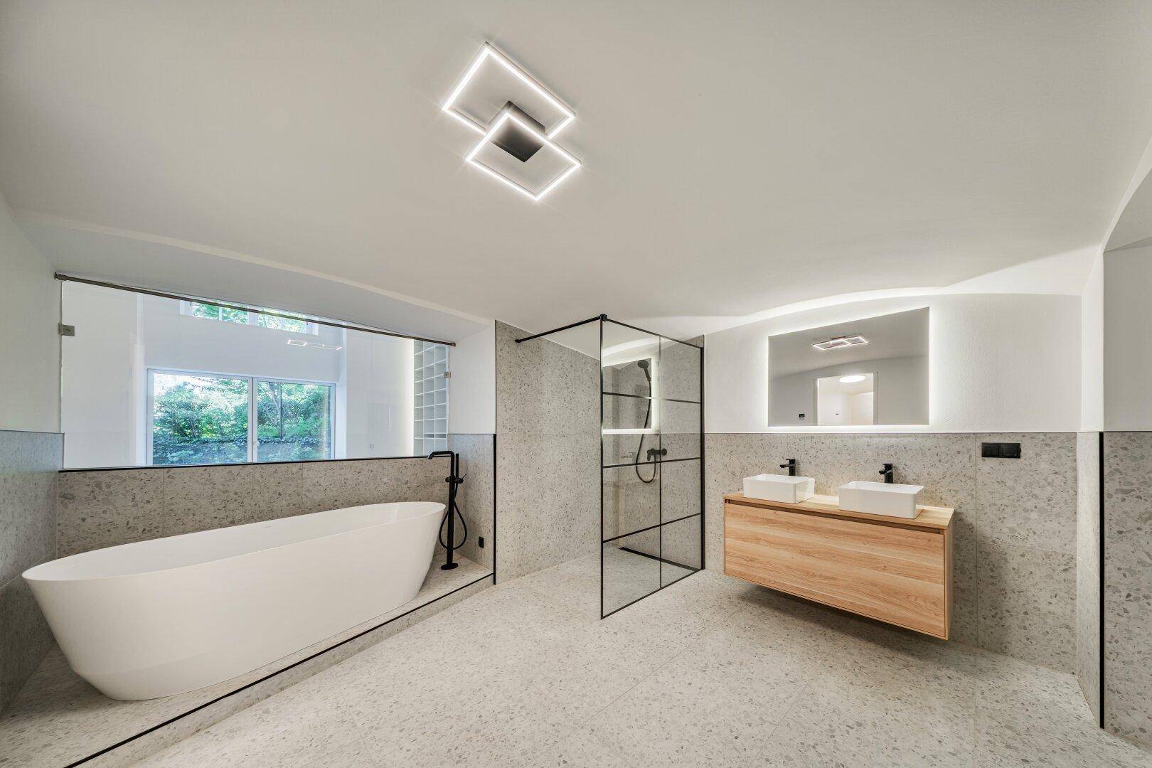 Elegantes Badezimmer mit freistehender Badewanne, begehbarer Dusche und Doppelwaschbecken auf Holzunterschrank.